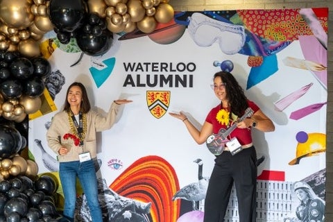 Alumni point to the Waterloo crest on a photo wall pop-up