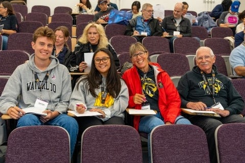 Alumni and their kids smile while sitting in a lecture hall