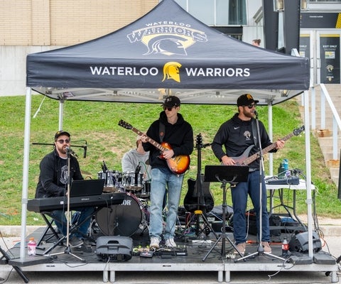 A band with two guitarists and a keyboardist play under a Homecoming tent