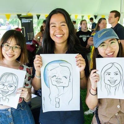 Three attendees each holding their caricature drawing and posing for the camera