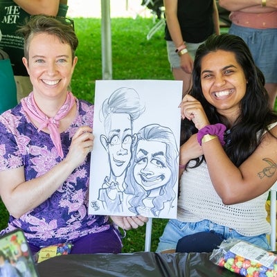 Two attendees holding a caricature drawing of them and posing for the camera
