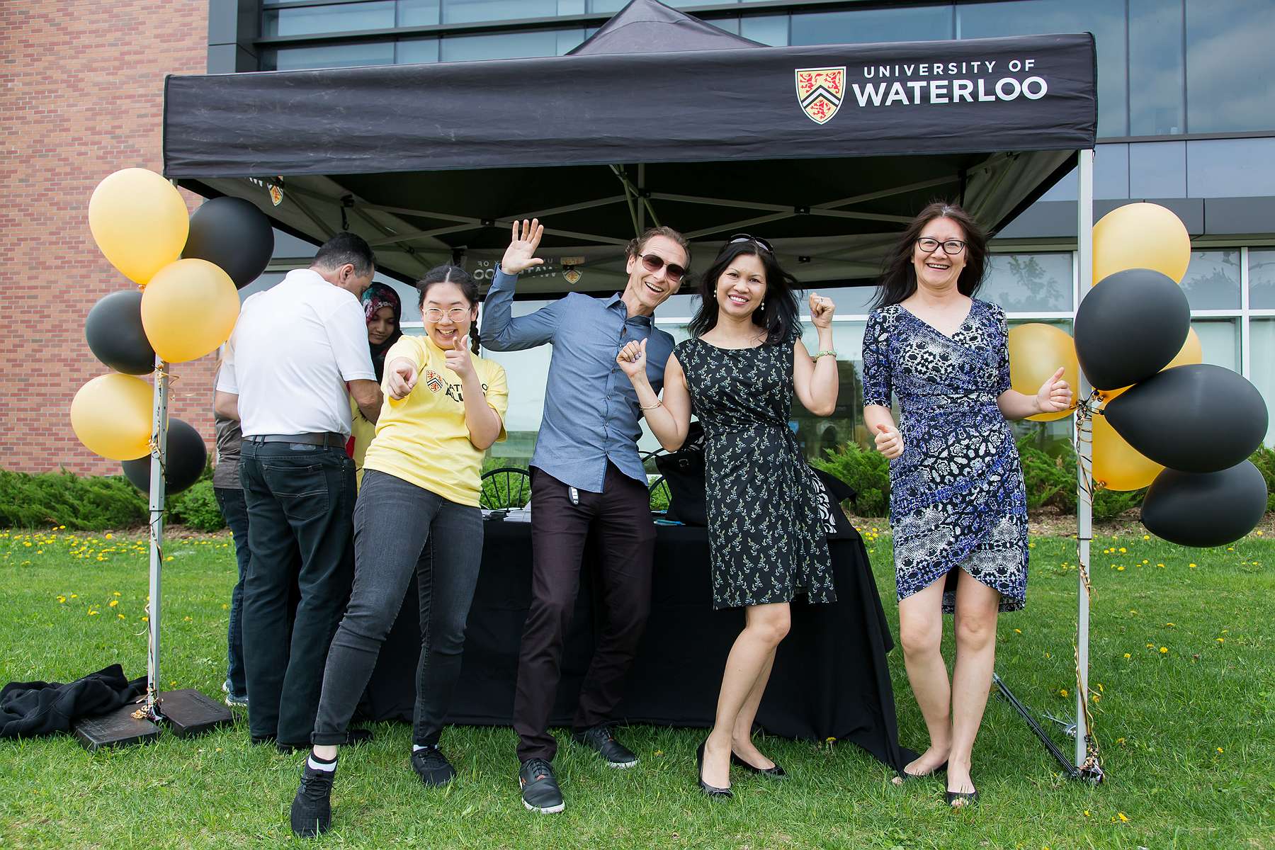 Alumni posing in front of a welcome tent with a volunteer