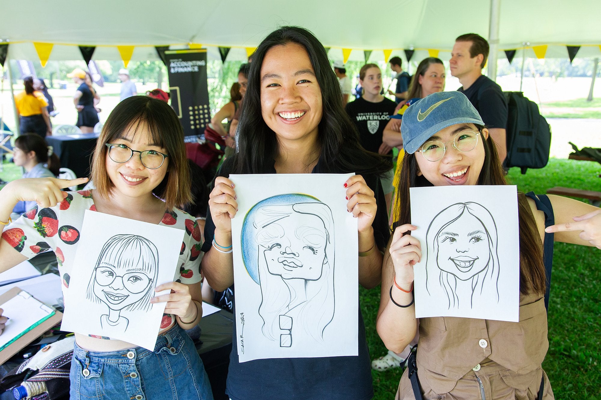 Three attendees each holding their caricature drawing and posing for the camera