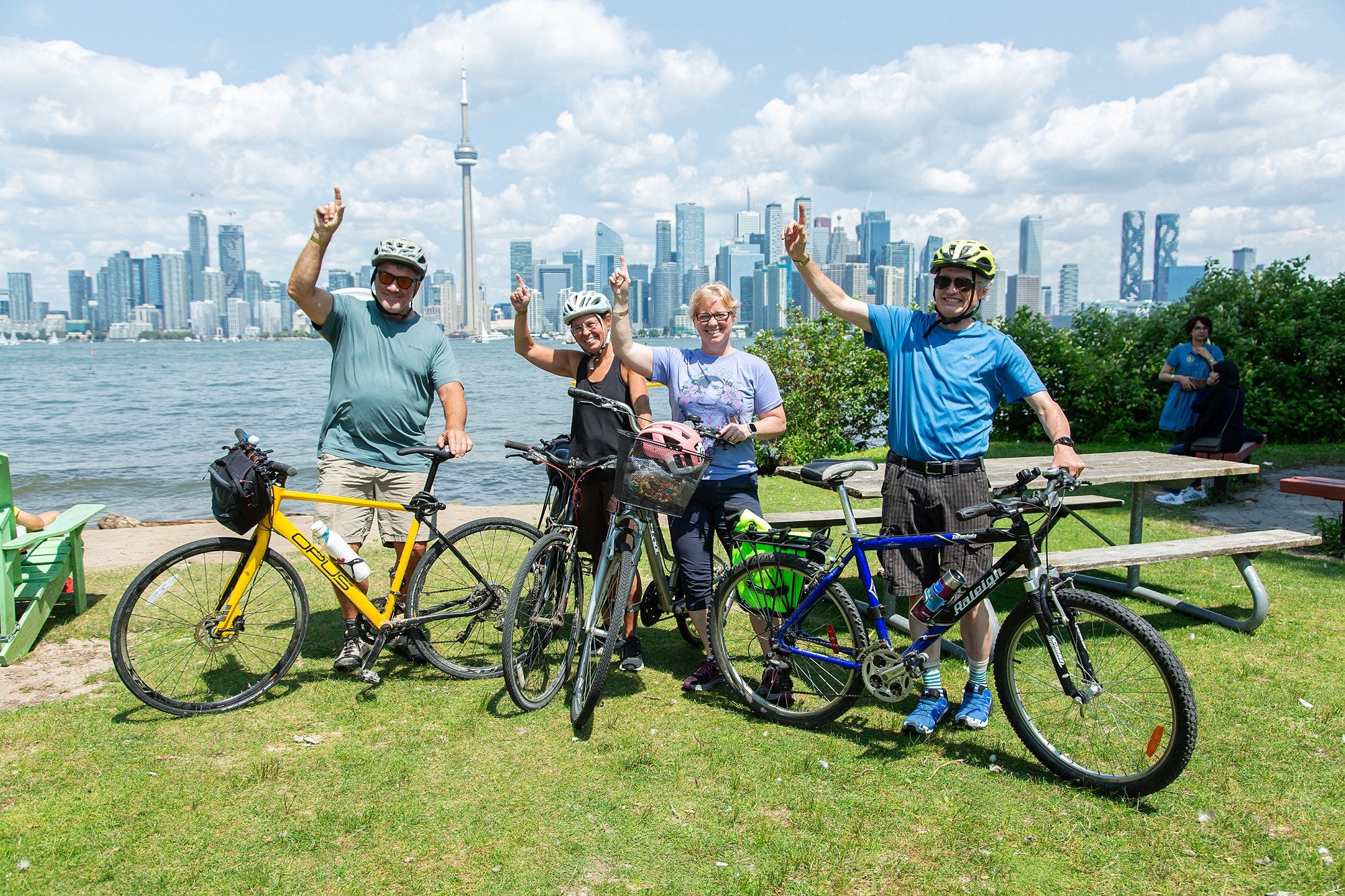 Four alumni with their bicycles pointing to the sky for a photo in front of the Toronto skyline