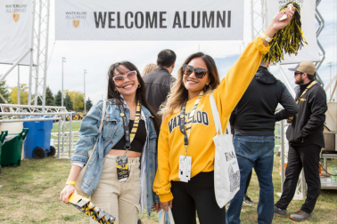 two ladies smiling in front of a sign reading "welcome alumni
