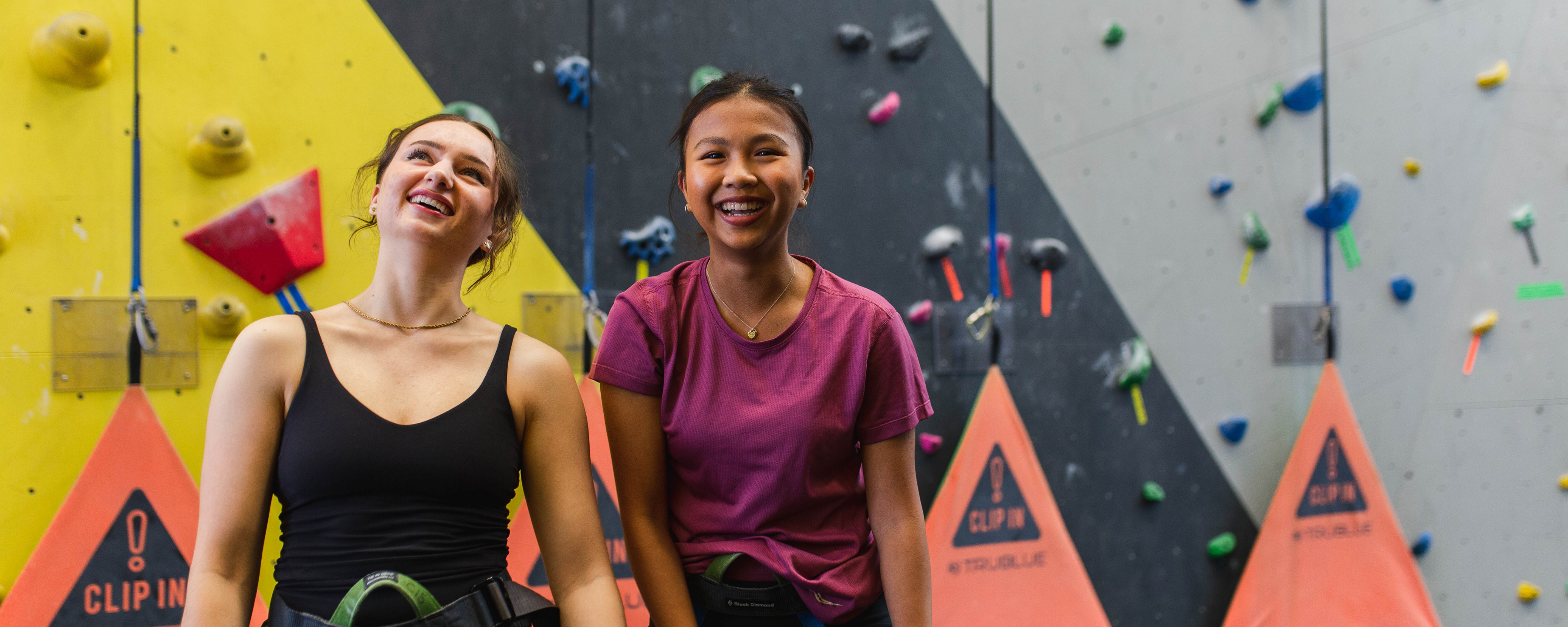 two girls smiling while standing in the rock climbing gym
