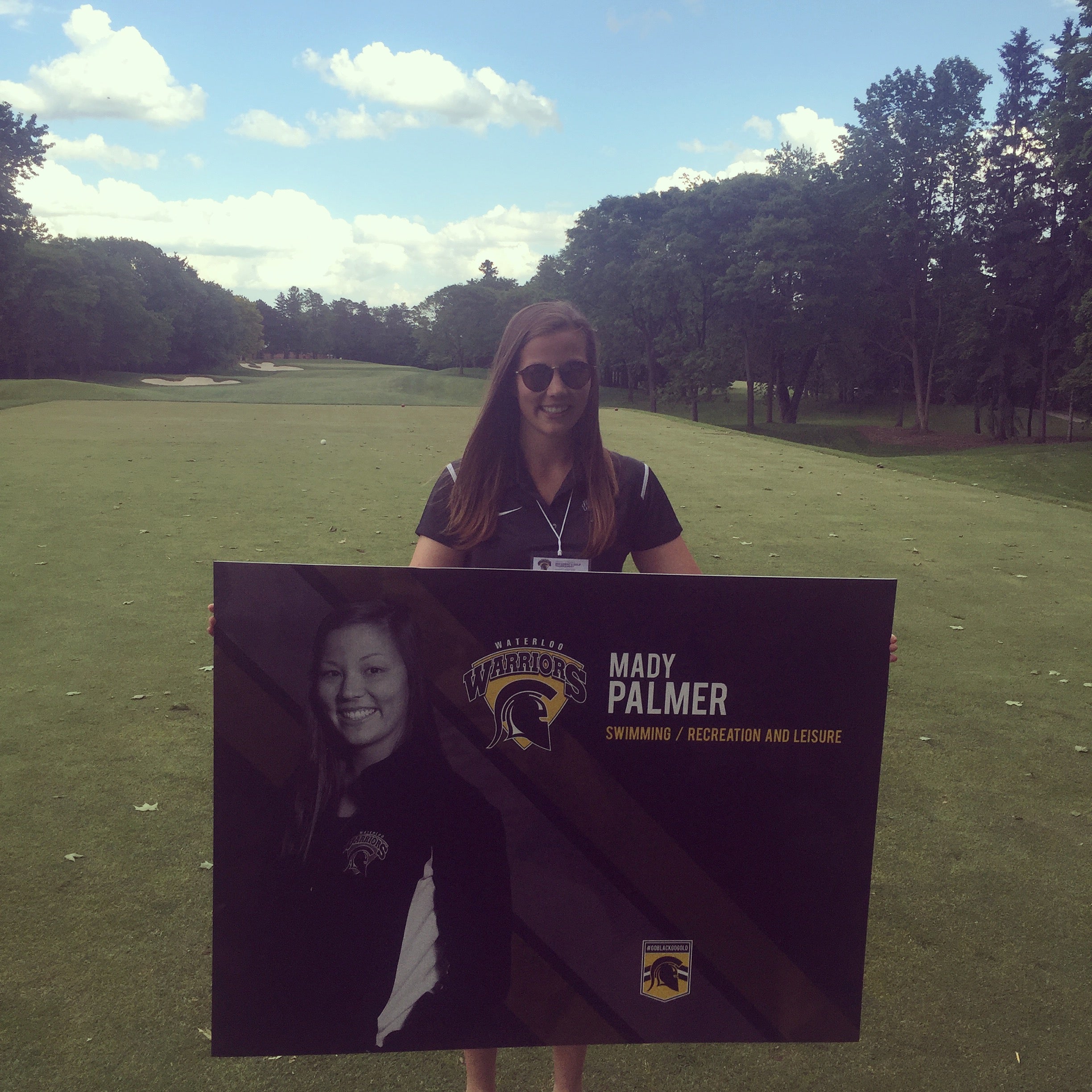 Mady Palmer on the golf course holding a sign with her face on it  