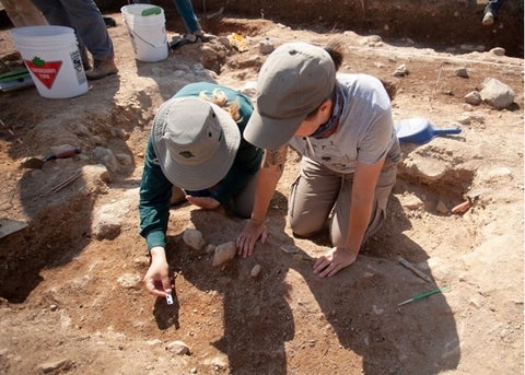 Two archaeologists word side by side examining an object uncovered in the dirt