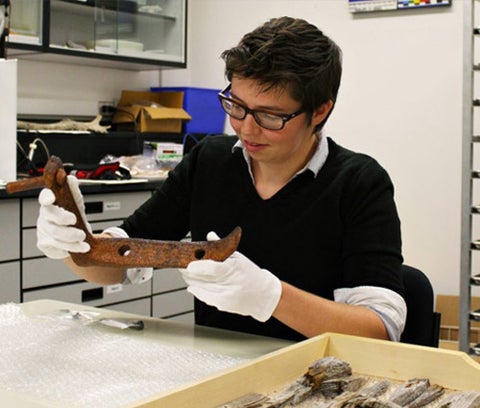 a graduate student examines a rusted metal part. There's a tray of wood fragments sittign nearby.