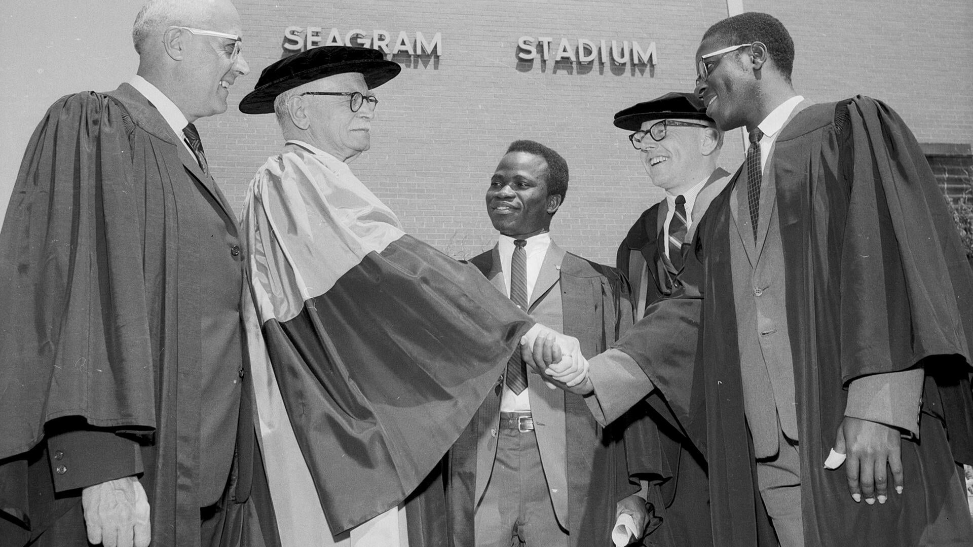 Black and white image of people in graduation gowns shaking hands