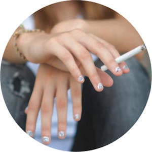 Teen's folded hands holding a lit cigarette.