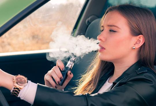 Female smoking e-cigarette in car.
