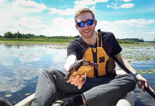Andrew MacDonald in a boat holding a turtle.