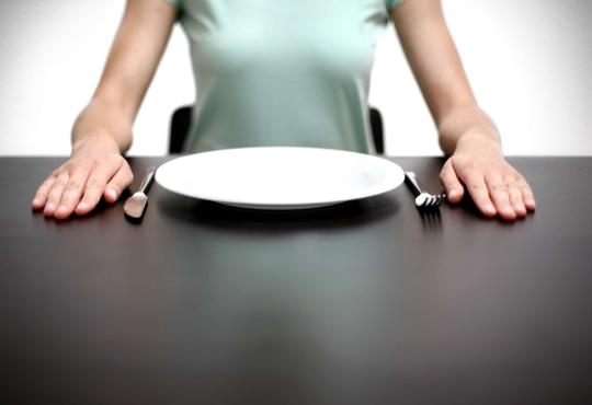 Person sitting at dinner table with empty plate.