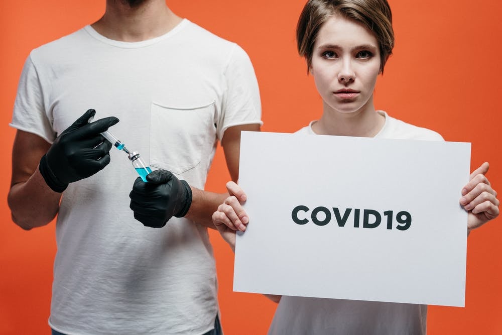 Young woman holding a sign with COVID19 to the right of a person holding a syringe