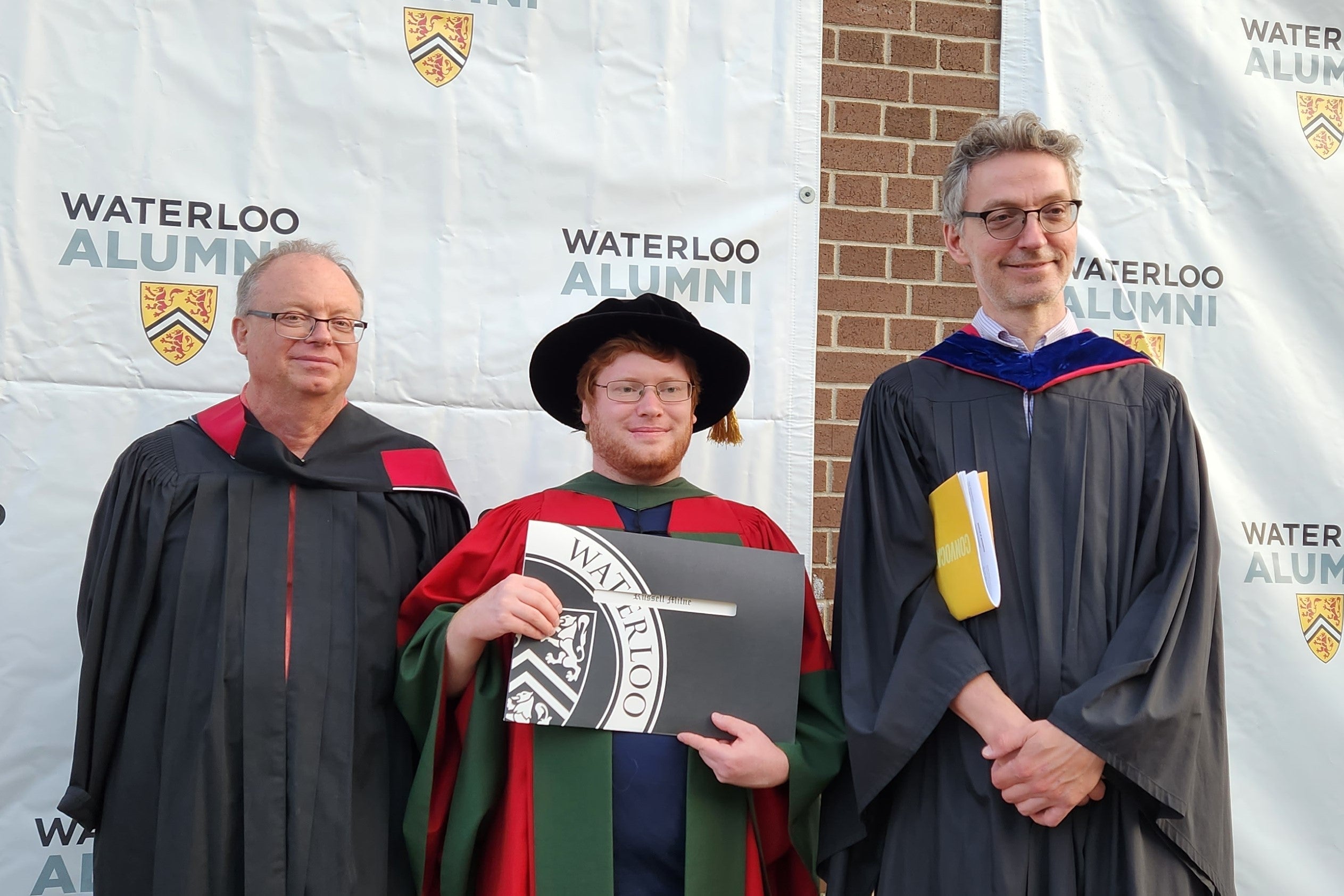 graduate student holding diploma with professors at convocation 