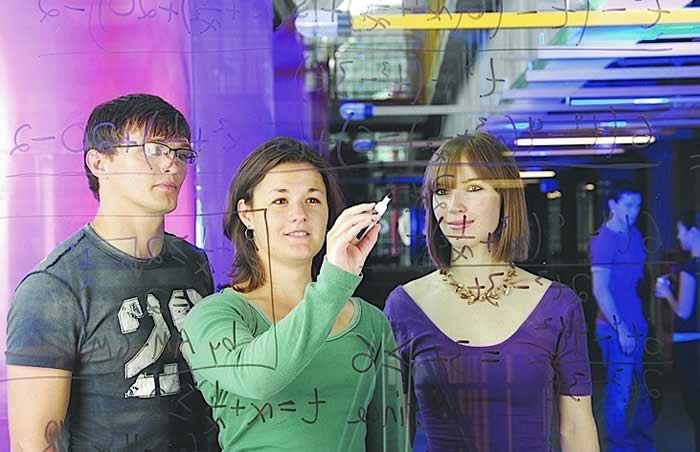 Students writing math equations on a glass board