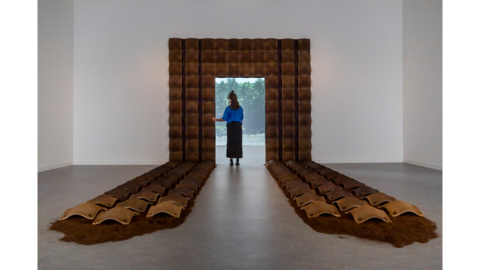 a woman stands in an doorway that is framed by a brown clay arch