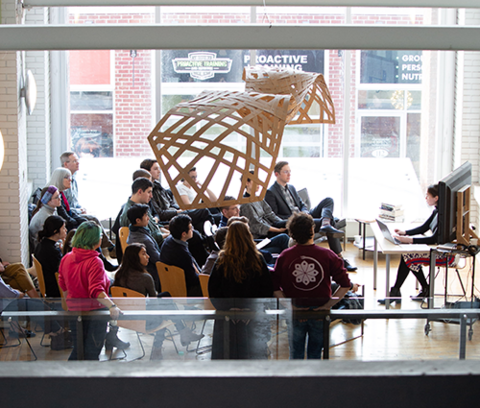 a student defends their architecture thesis in front of an audience in the school of architecture atrium