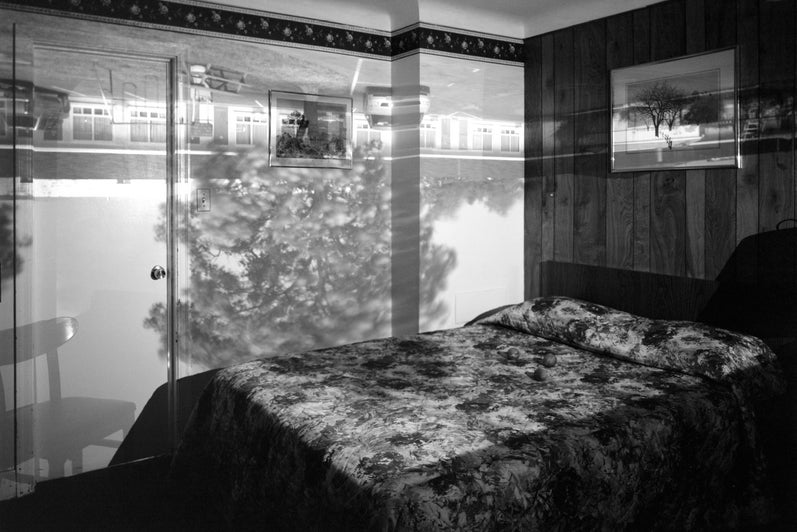 A black and white photograph of a bedroom with an upside down image projected onto the walls.