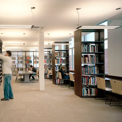 A male student is picking books from the bookshelves and other students are reading at the back