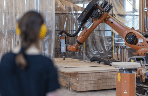 Woman watches a robotic arm cutting wood