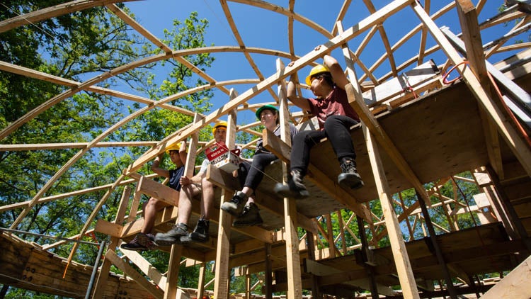 students taking a break sitting on scaffold inside arbor