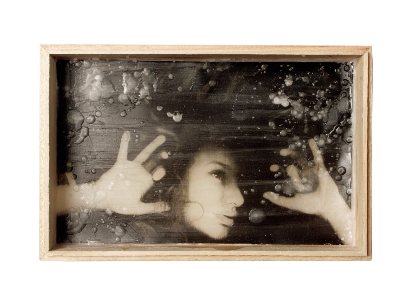 A framed artwork of a photograph/drawing of a girl underwater, the bubbles are represented with melted wax ontop of the image.