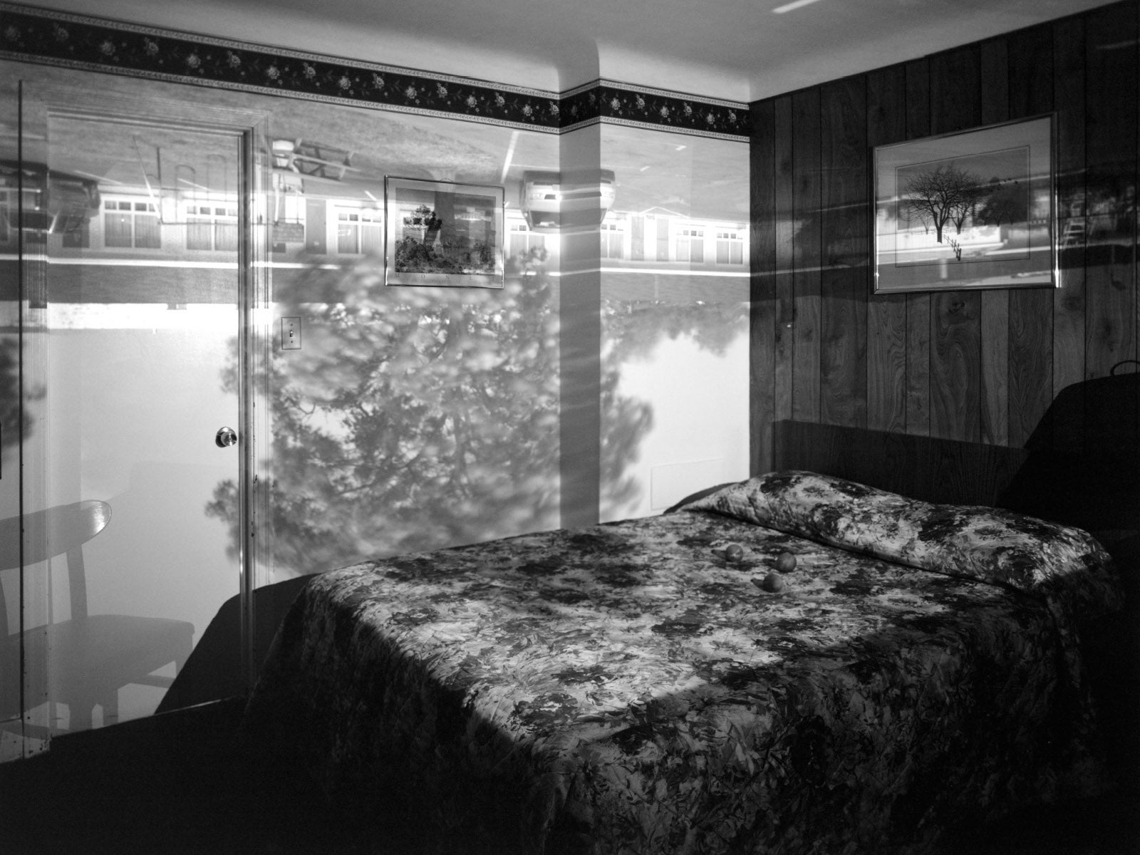 A black and white photograph of a bedroom with an upside down image projected onto the walls.
