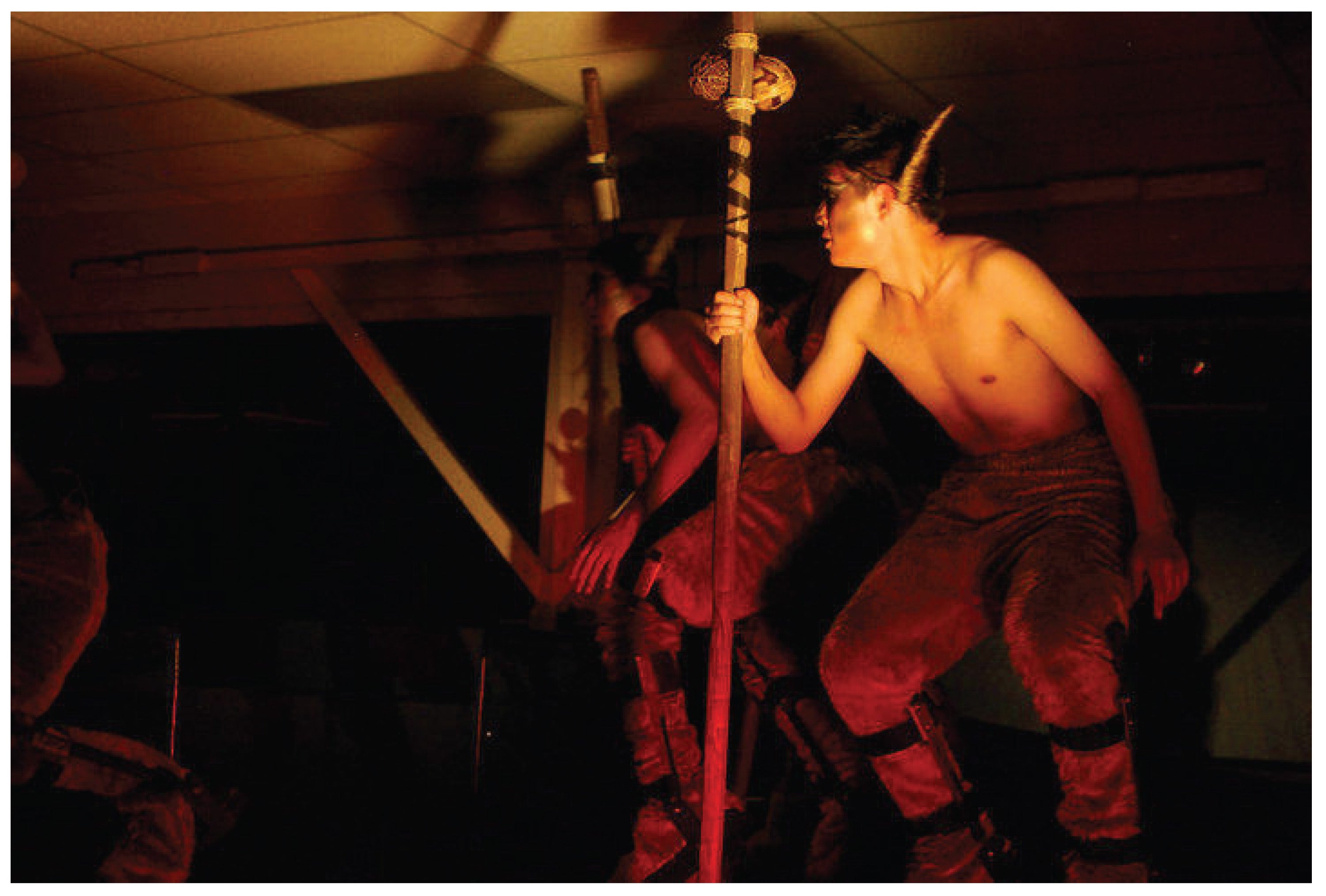 A photograph of savage looking people holding wooden staffs looking off to the side. The shot is made with limited lighting.