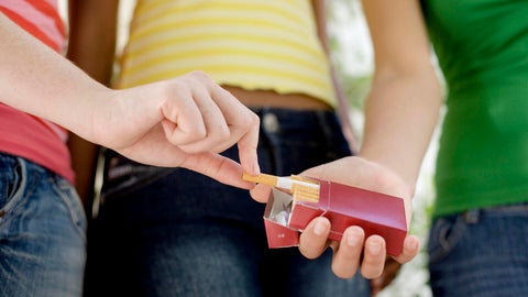 Teenage girl taking cigarette from friend cigarette pack