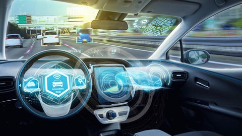 Interior view of an autonomous vehicle driving on a highway, showing digital dashboards and augmented reality displays highlighting cars, speed, and navigation data.