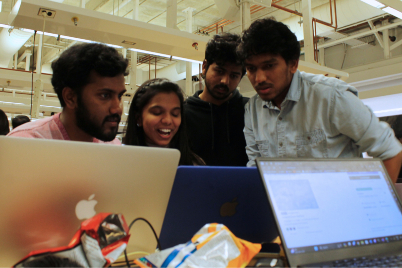 A team of four work on their project, crowded around a laptop