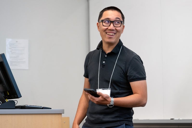 A speaker smiles while presenting at the front of the room