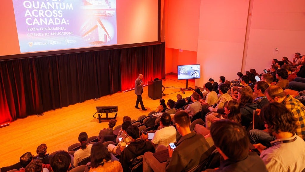 Researchers and students gather around advanced quantum equipment inside a laboratory at the University of Waterloo’s Institute for Quantum Computing, surrounded by wires, lasers, and scientific instruments.