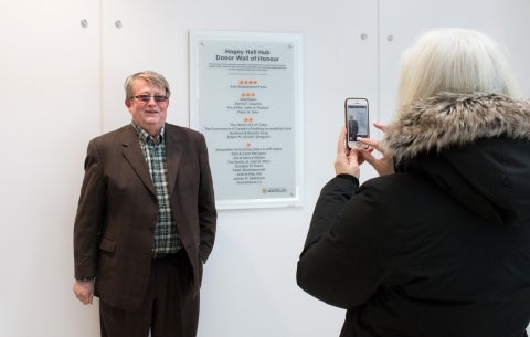 Professor emeritus smiles for camera beside plaque