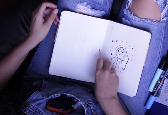 person drawing in notebook on lap