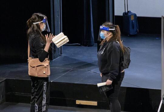 Two actors with masks and facesheilds rehearse in theatre
