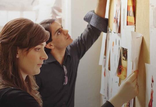 Two enterpreneurs contemplate drawings of their ideas on a bulletin board