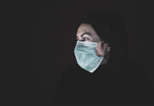 A lone woman wearing a mask against a dark background