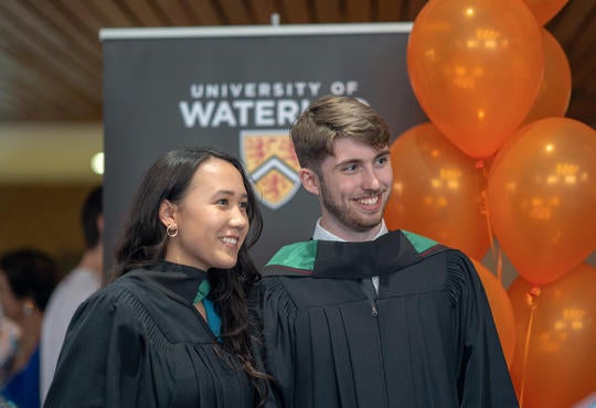 two students smile in graduation robes