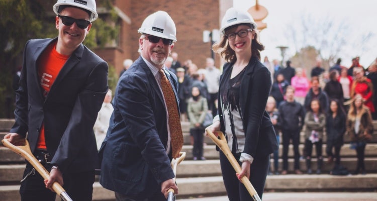 dean of arts and two students with shovels and hard hats at groundbreaking ceremony
