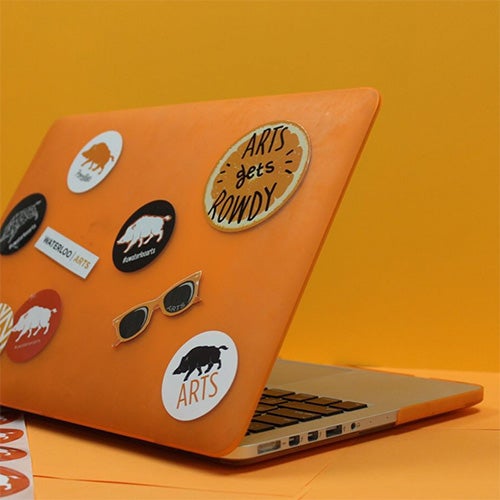 A laptop with an orange case and Arts stickers on it