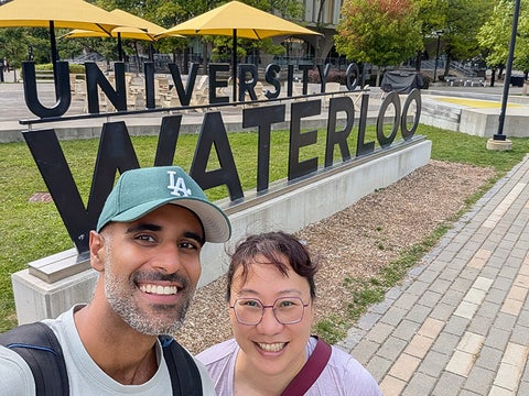 Phoebe Wong and Arwin Dhingra take a selfie next to the University of Waterloo ign