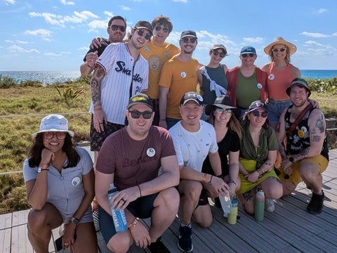 A group of 12 friends smile on a boardwalk in Mexico