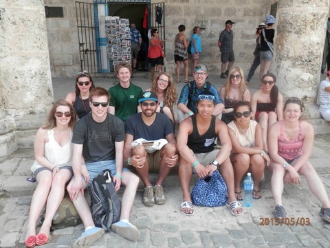 A group of 12 friends sit on a cobblestone street in Cuba