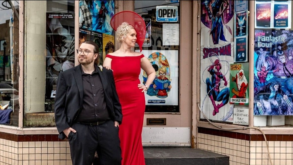 A man in a black suit and a woman in a red gown and big hat outside a local Waterloo comic book store