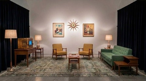 A mock up of a living room with armchairs, 70s-era tables and a piece of art that looks like an old television set