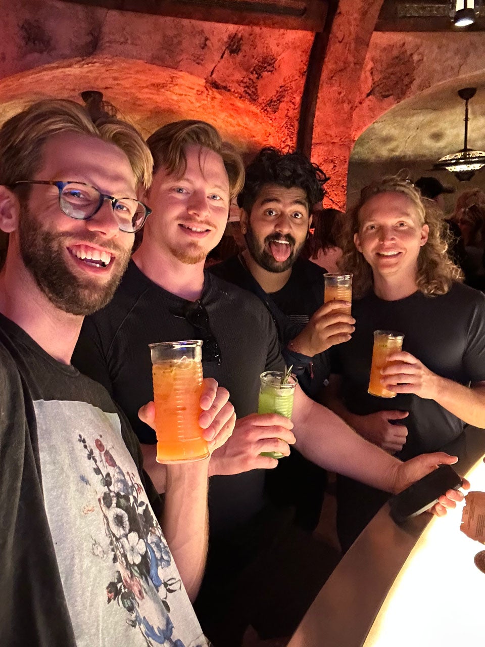 Four friends smile holding beers
