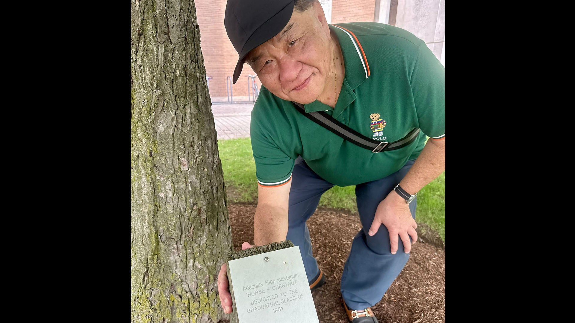 Michael Tee next to a tree and plaque along Alumni Lane